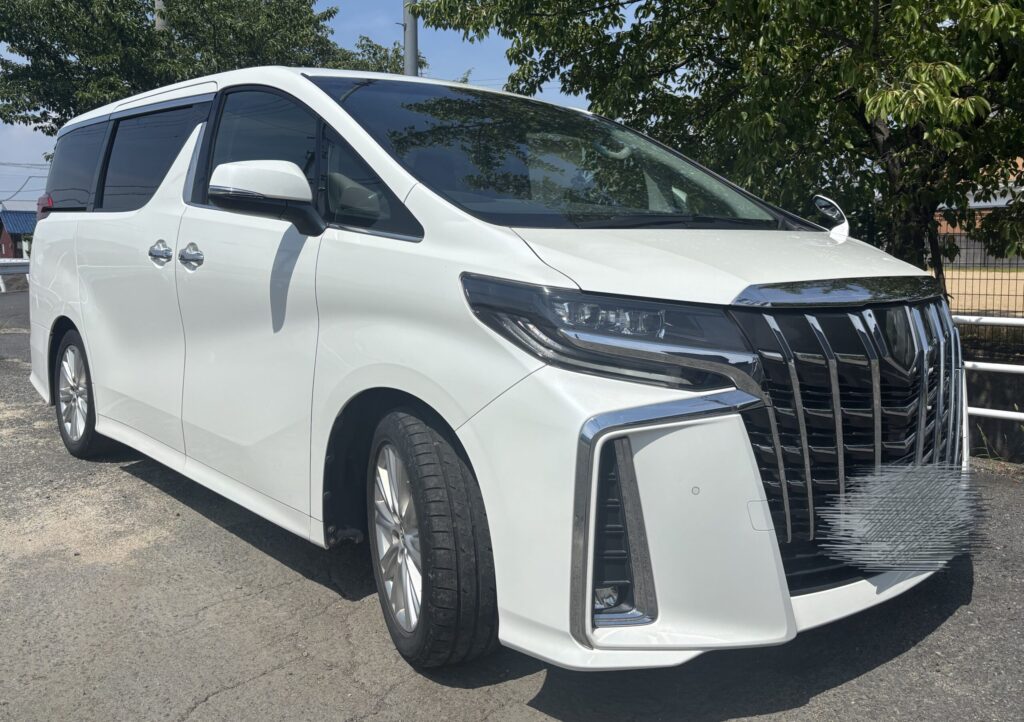 晴天の屋外に駐車した白い30系後期アルファードを右斜め前から撮影した外観
