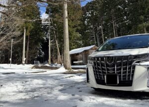 雪が積もる森林に停めた白い30系後期アルファードのフロントグリル
